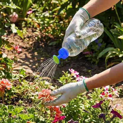 Gloved hands hold a clear plastic bottle with a blue and green sprinkler cap, watering pink flowers in a garden.