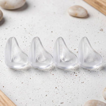 Four clear, rounded silicone corner protectors are lined up on a speckled white surface with light pebbles.