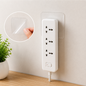 A hand peeling a clear adhesive square from a wall, next to a white power strip mounted with another square.