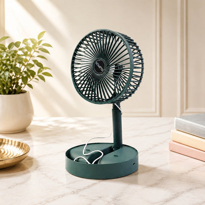 A dark green telescopic foldable mini USB desk fan on a marble desk next to a plant and books.