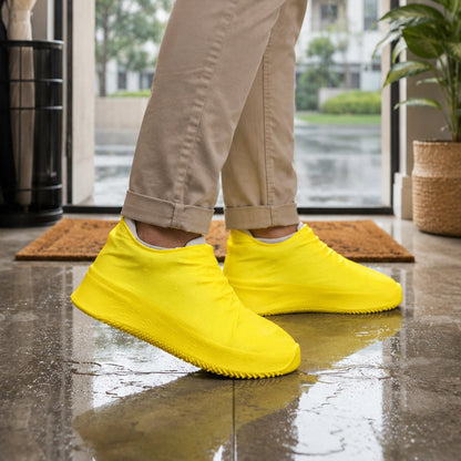 A person wearing khaki pants and bright yellow silicone shoe covers stands on a wet tiled floor, with water splashes.