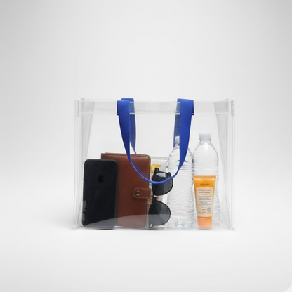 A clear PVC tote bag with blue handles holds a phone, wallet, sunglasses, water bottle, and sunscreen.