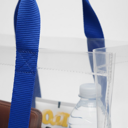 A close-up of the clear PVC tote bag shows the blue fabric handles and a water bottle inside.