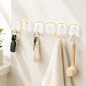 Six transparent adhesive hooks with gold borders holding keys, a towel, and a brush on a white wall.
