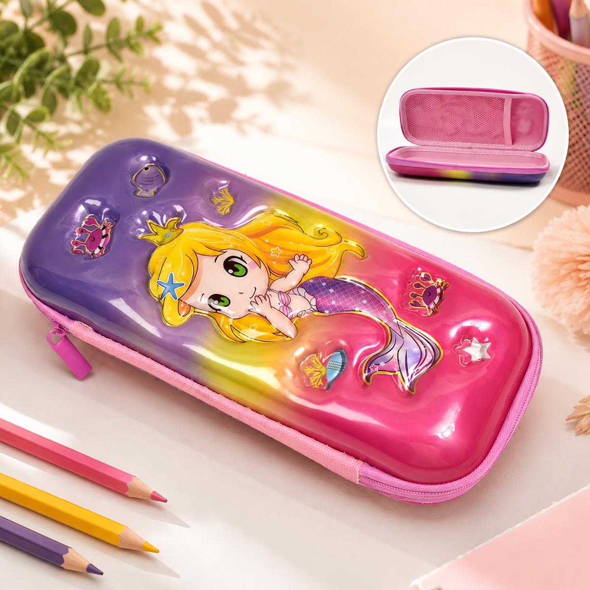 A vibrant mermaid-themed hard shell pencil case with a pink zipper, next to colored pencils. An inset shows the open case.