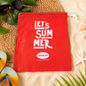 A red drawstring bag with "LET'S SUMMER" and Havaianas logo, surrounded by sunglasses, flip-flops, and beach decor on sand.