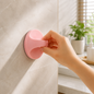A hand pulls a pink self-adhesive handle attached to a light gray tiled wall in a bathroom setting.