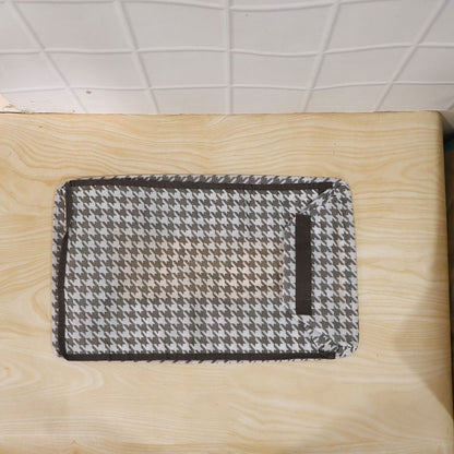 A gray and white houndstooth fabric organizer lies flat on a light wood surface, with a dark brown border.
