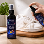 A hand sprays Shynex shoe cleaner onto a very dirty white sneaker next to a full bottle of cleaner.