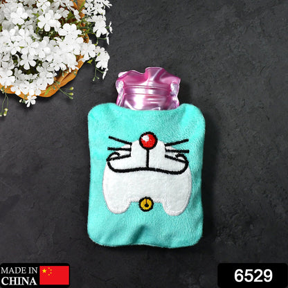 A light blue hot water bag with a Doraemon face design lies on a dark surface next to white flowers.