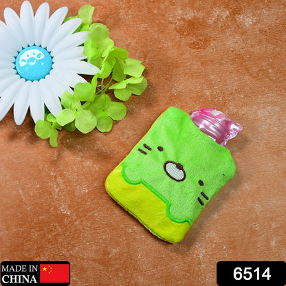 A green and yellow kitty hot water bag lies next to a white flower and green leaves on a brown surface.