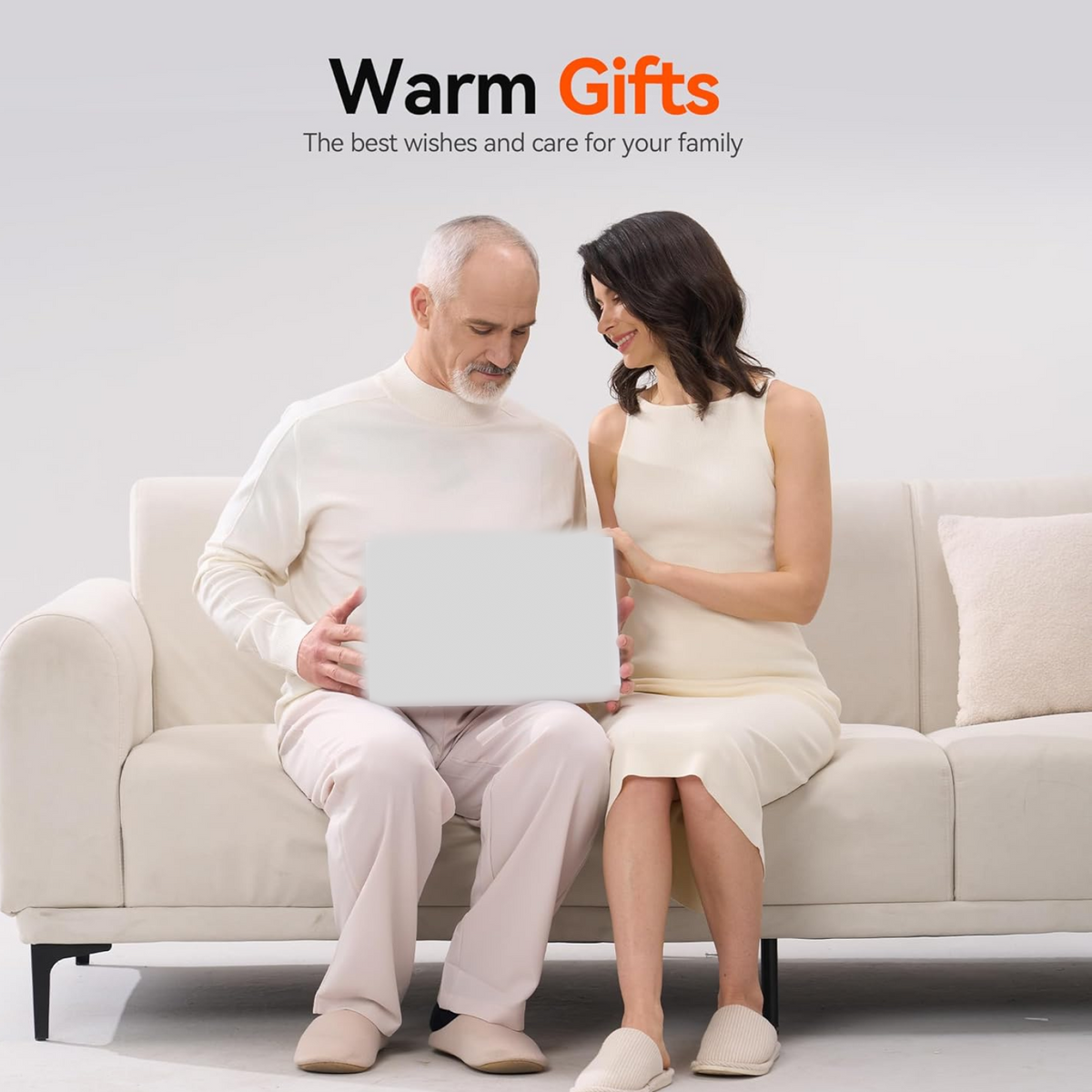 A man and woman sitting on a couch, smiling and looking at a white gift box they are holding.
