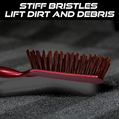 A close-up of the red and white handled brush with brown bristles on a dark textured surface, with text about stiff bristles.