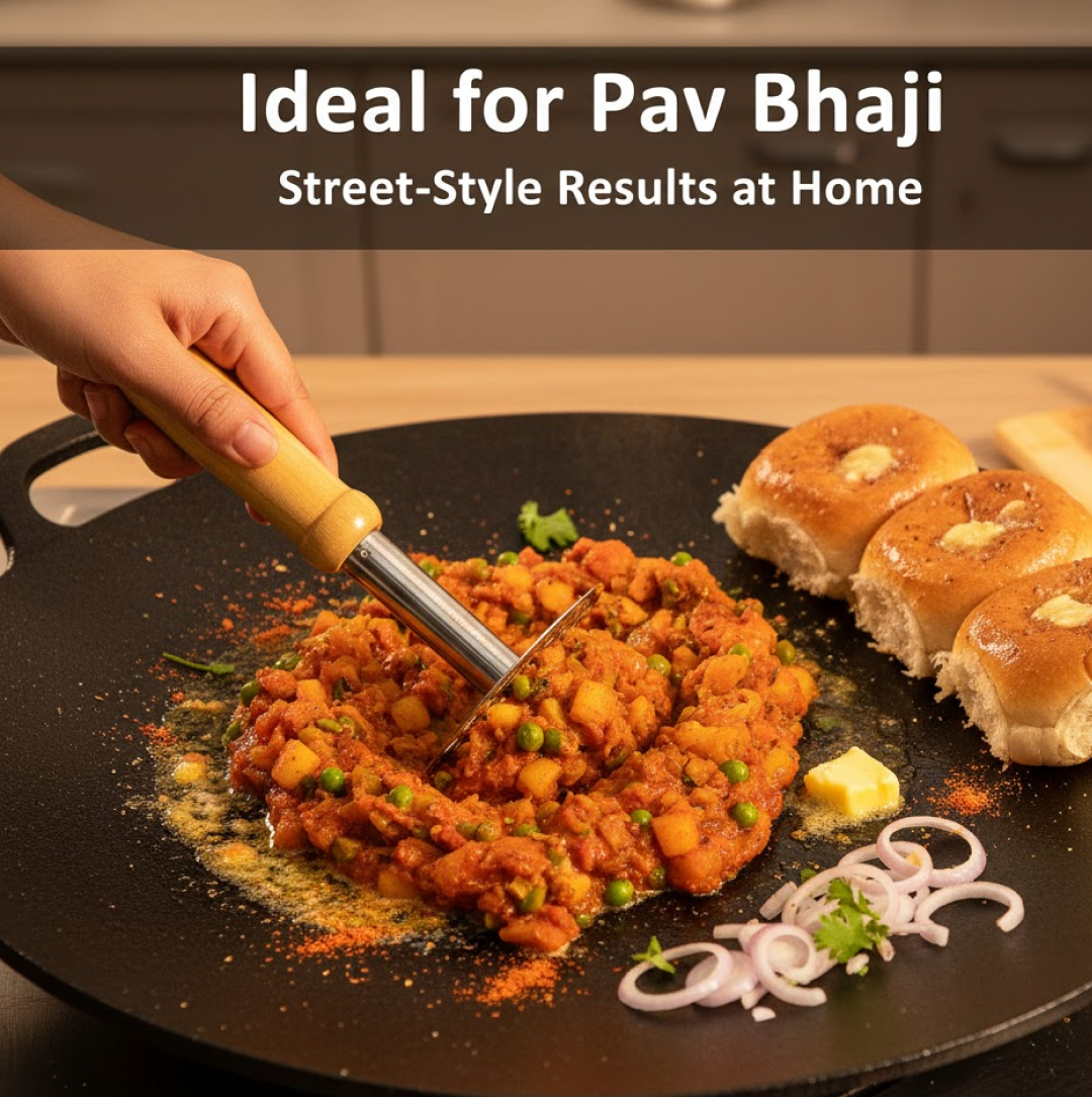 A hand uses the masher to press down on a vibrant orange pav bhaji mixture on a black griddle, with buns and onions nearby.