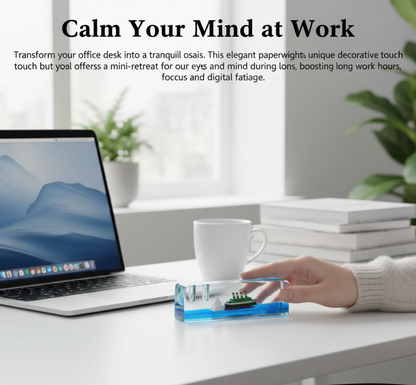 A hand holds a clear liquid motion paperweight with a ship and iceberg on a white desk next to a laptop and coffee cup.