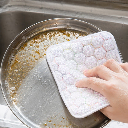 Hand scrubbing a dirty pan with a white honeycomb-patterned cleaning cloth, creating suds in a kitchen sink.