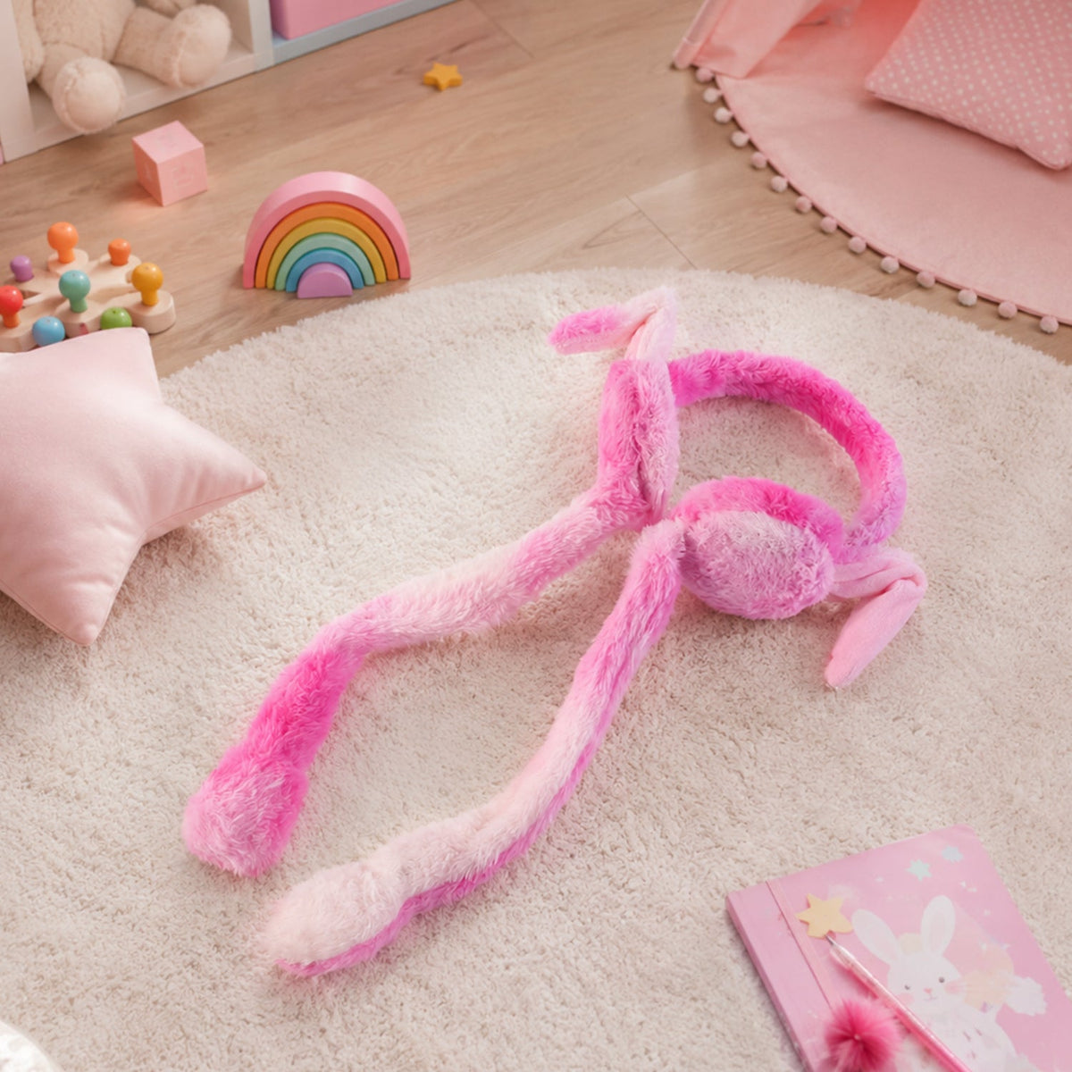 Pink and white plush bunny earmuffs with long tails lying on a white fluffy rug in a child's room with pink accessories.