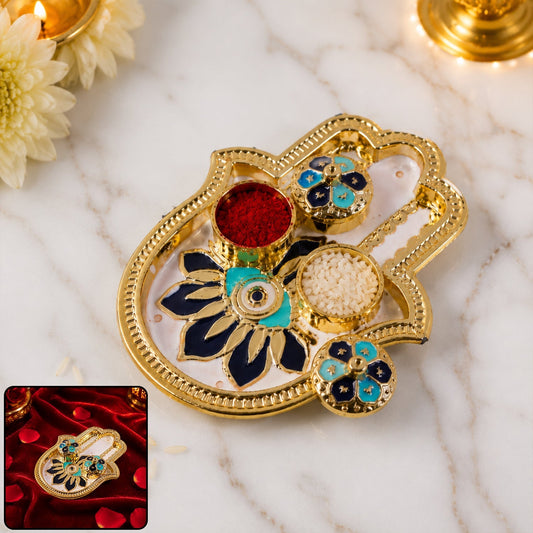 Golden hamsa hand thali with red kumkum and white rice in small blue and black enamel bowls.