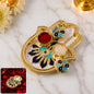 Golden hamsa hand thali with red kumkum and white rice in small blue and black enamel bowls.