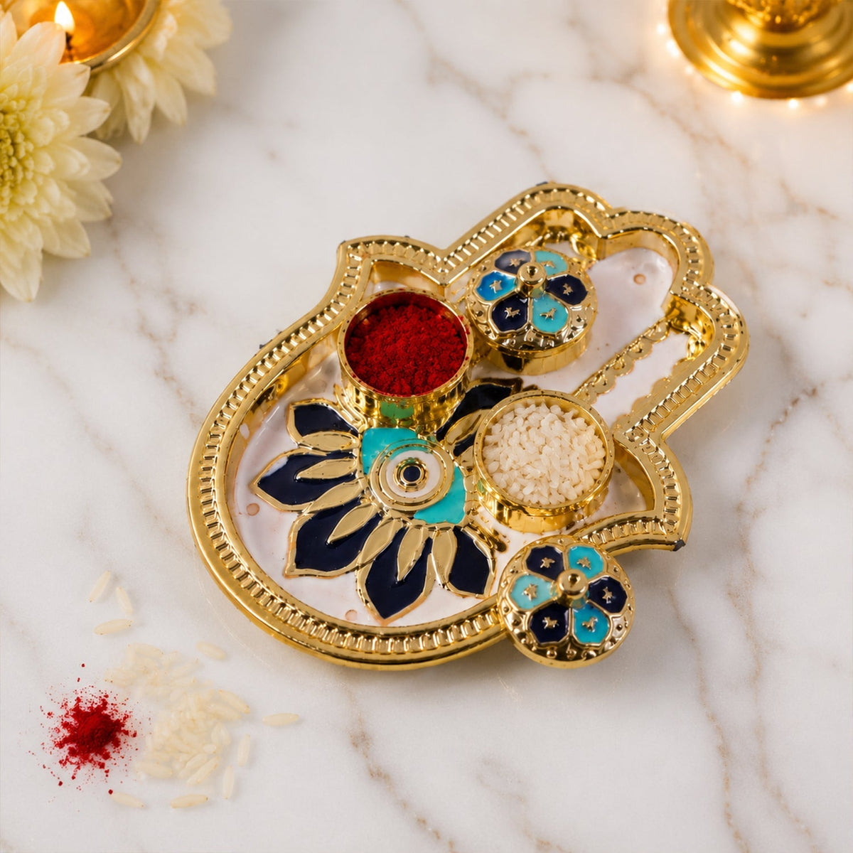 Golden hamsa hand thali with red kumkum and white rice, blue and black enamel, with scattered grains.