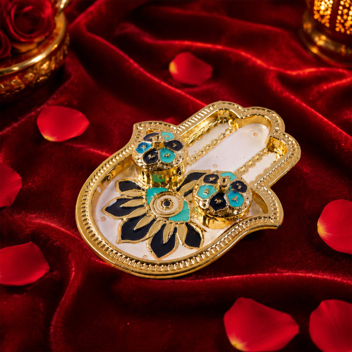 Golden hamsa hand thali with blue and black enamel details, resting on a rich red velvet fabric with petals.