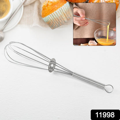 A silver spring coil whisk is displayed on a white surface with a blurred background of baked goods and a person whisking