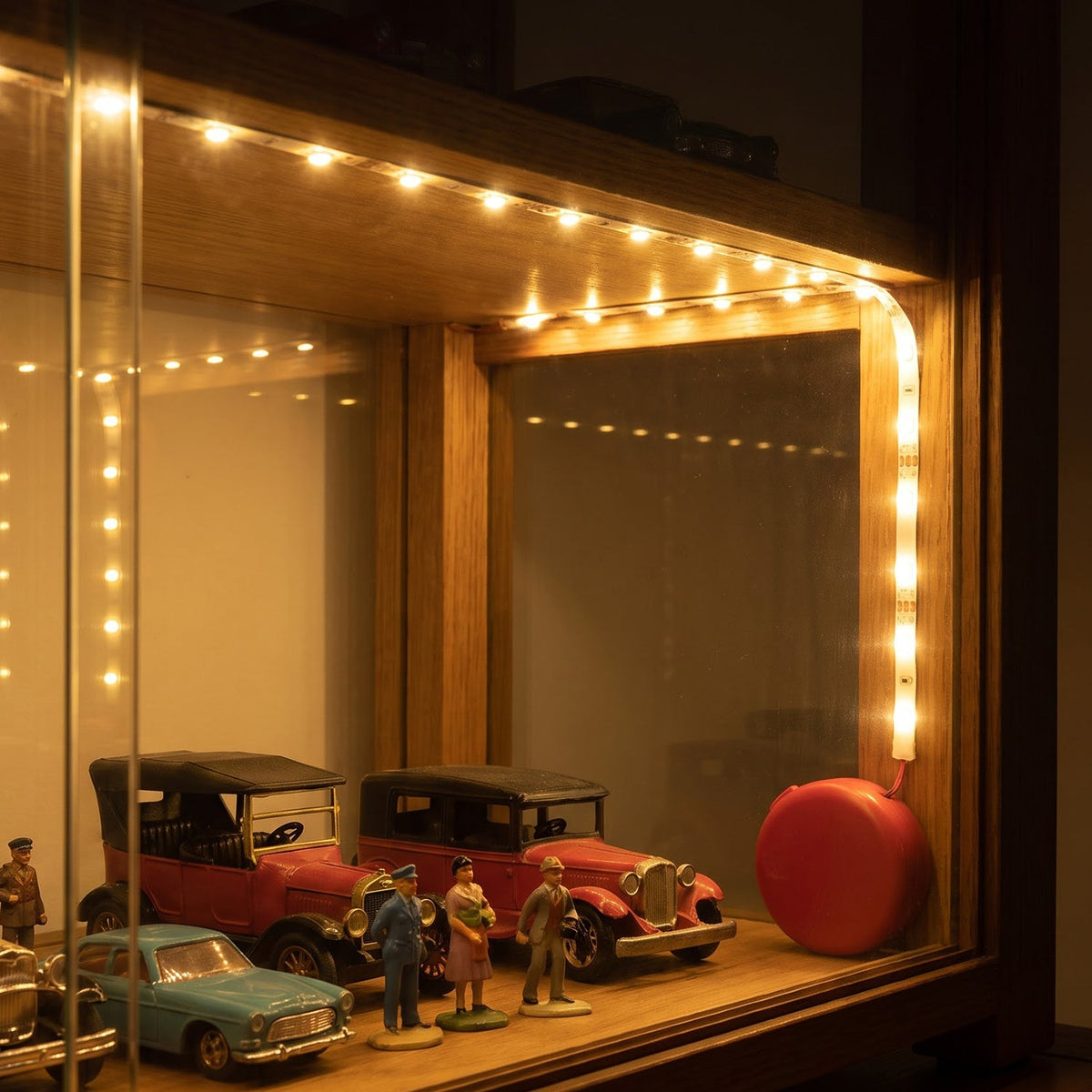 The illuminated LED strip lights provide ambient lighting for a collection of miniature cars in a wooden display case.