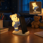 A glowing yellow bear phone holder with blue overalls on a desk at night, holding a phone.