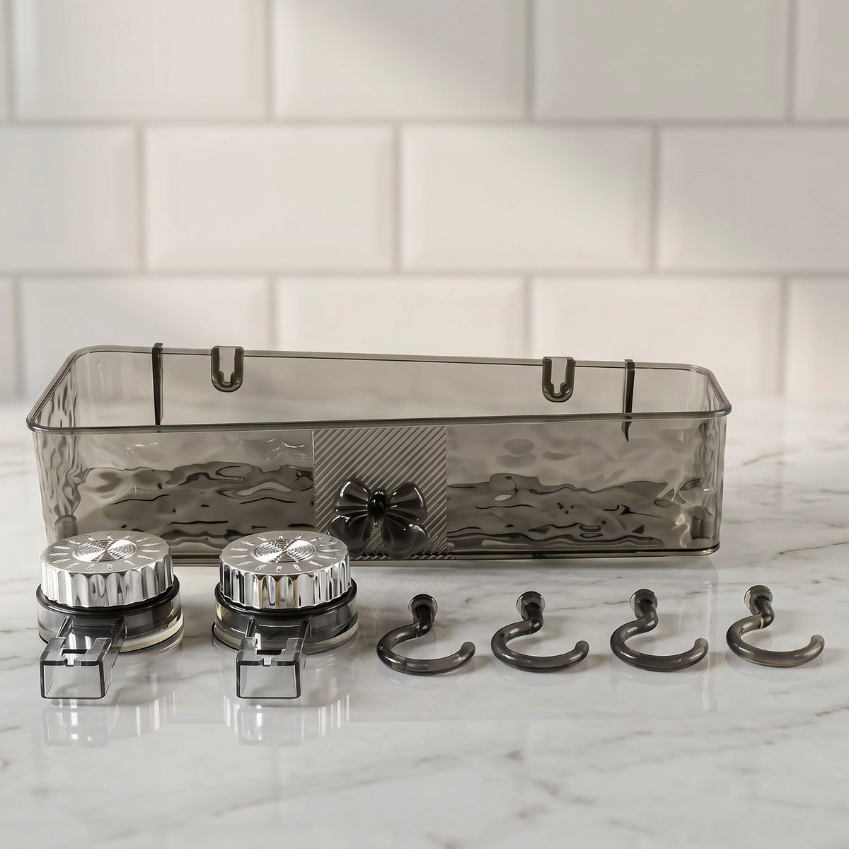 A clear grey plastic caddy, two silver suction cups, and four grey hooks are arranged on a white marble surface.