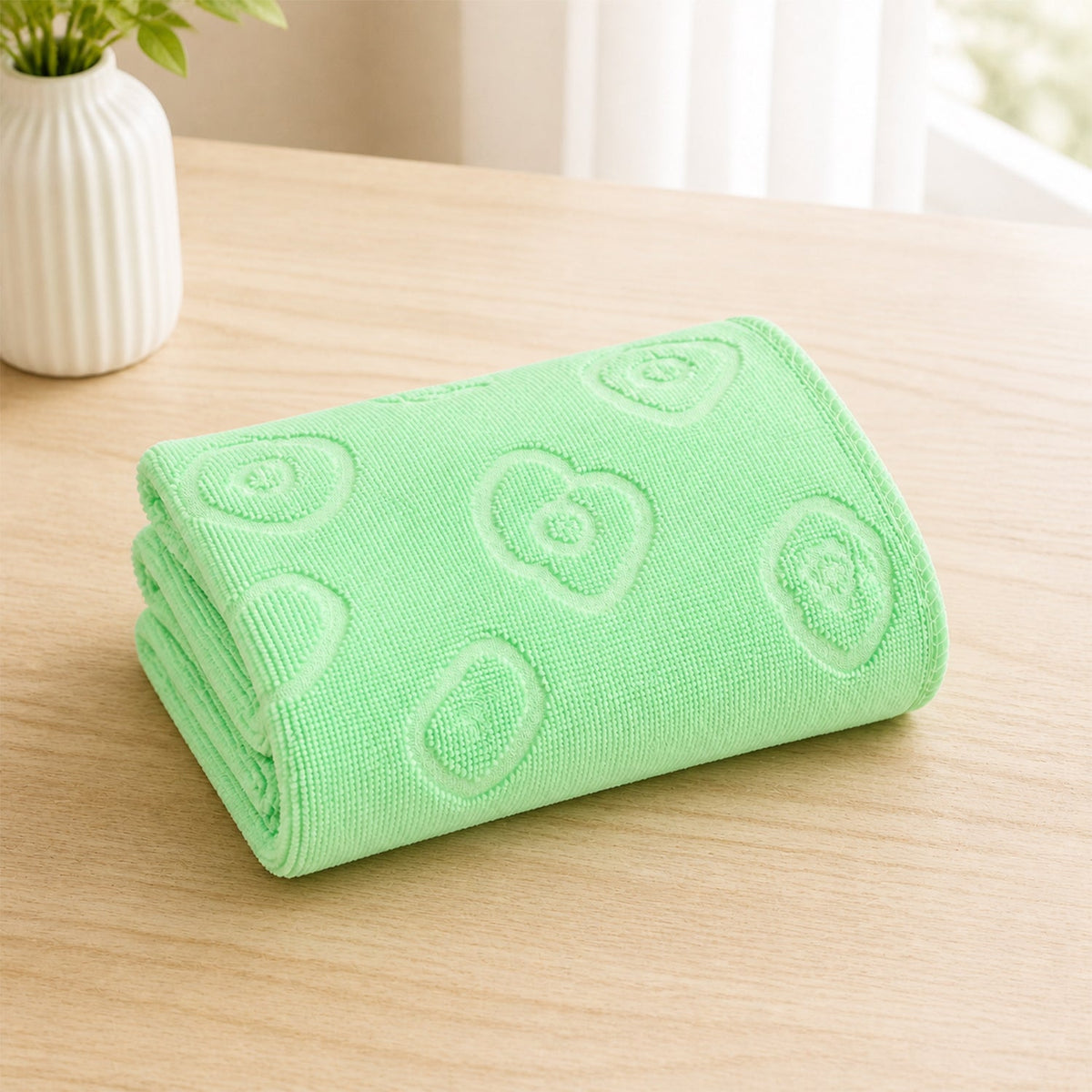 A light green folded microfiber towel with embossed heart and flower patterns on a wooden surface.