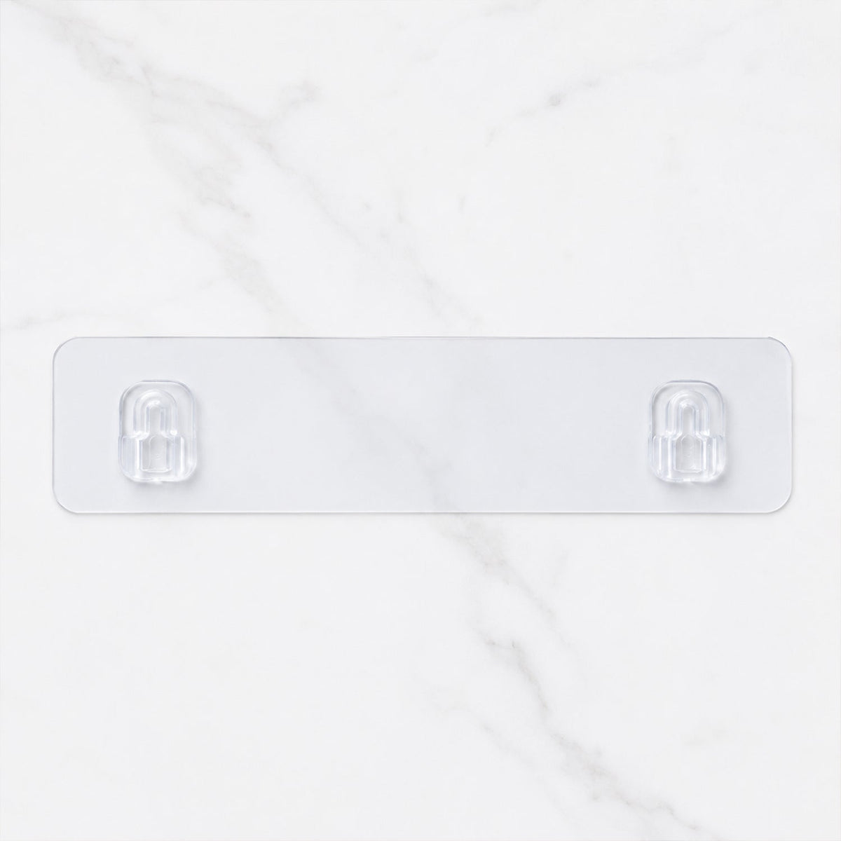 A clear adhesive wall hook strip with two hooks against a white marble background.