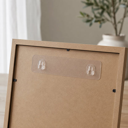 A close-up of a clear adhesive wall hook strip applied to the back of a light brown picture frame.