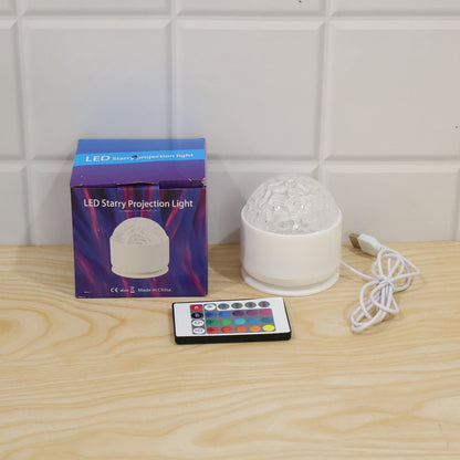 A white LED projection light, its box, and a remote control on a light wooden surface against a white tiled wall.