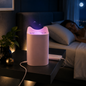 A pink cat-eared mosquito lamp glows purple on a nightstand next to a sleeping woman in a dark room.