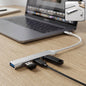 A silver Type C to four-port USB hub connected to a laptop, with a USB drive and cable plugged in