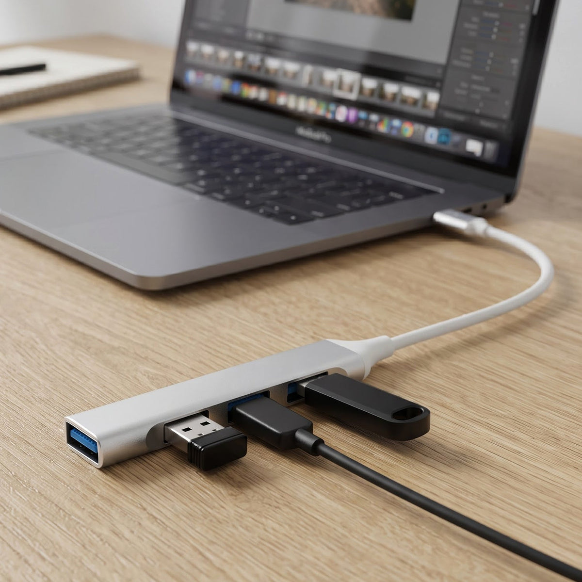 A silver Type C to four-port USB hub connected to a laptop, with a USB drive and cable