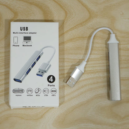 Silver 4-port USB hub next to its white packaging box on a light wooden surface.