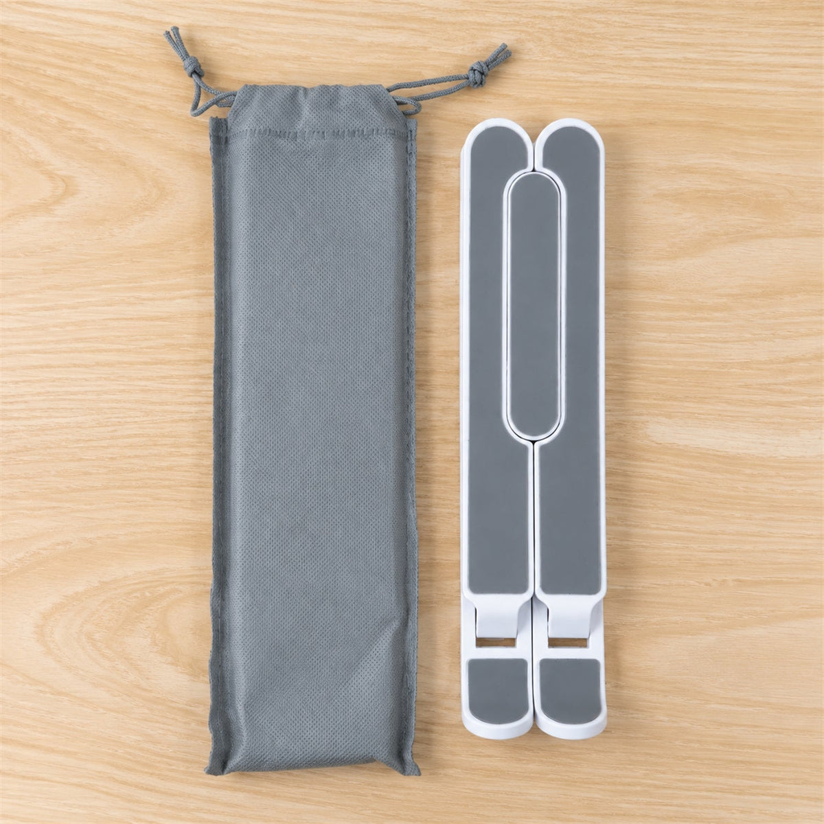 Folded white and gray laptop stand next to a gray drawstring carrying pouch on a wooden surface.