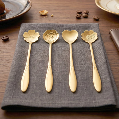 Four gold decorative spoons with flower and heart shapes are neatly arranged on a dark gray napkin.