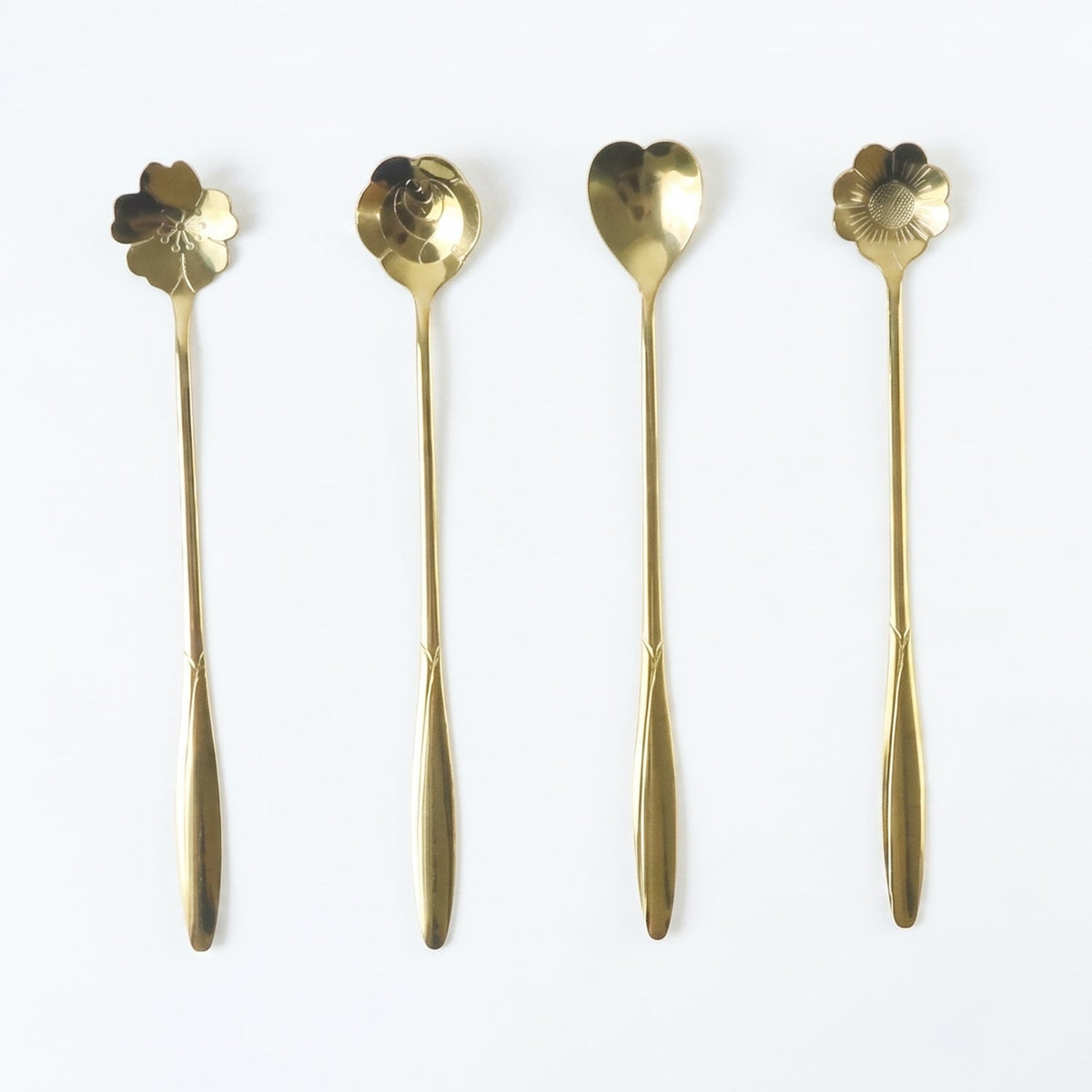 Four long-handled gold decorative spoons with flower and heart shapes arranged on a white background.