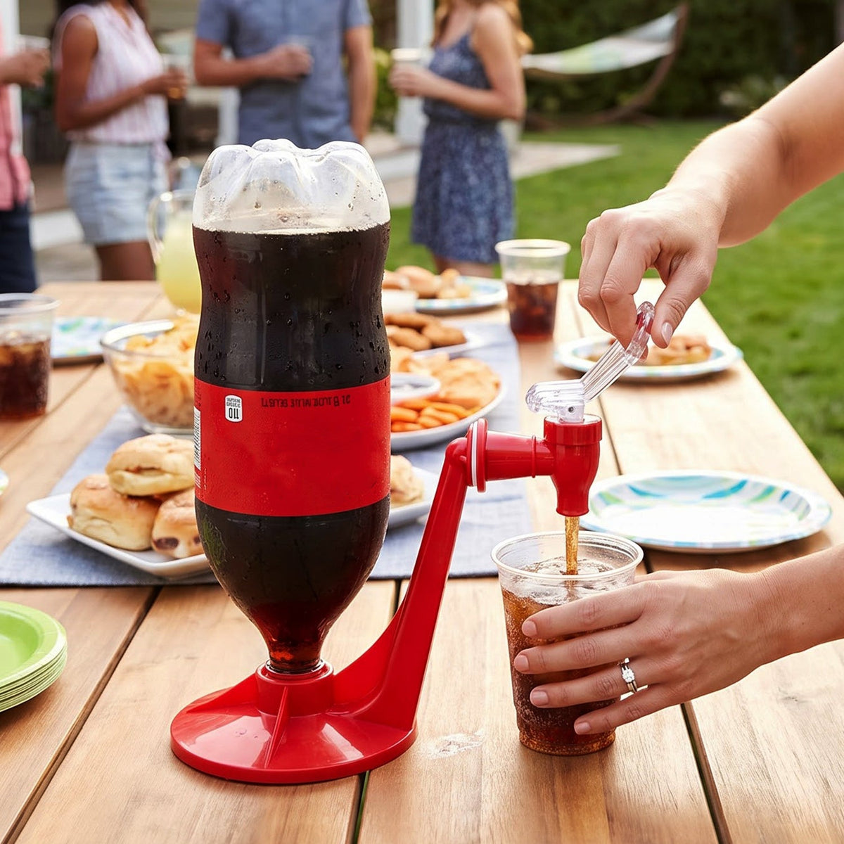 A person dispenses dark soda from a large bottle in a red plastic dispenser at an outdoor gathering.