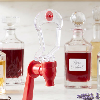 Close-up of the clear and red plastic tap of a beverage dispenser, with decorative glass bottles in the background.