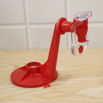 A red plastic beverage dispenser with a clear tap, resting on a light wooden surface against a white tiled wall.