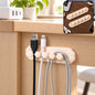 Beige flower-shaped cable organizer clip with five slots holding black, white, and grey cables under a wooden desk.