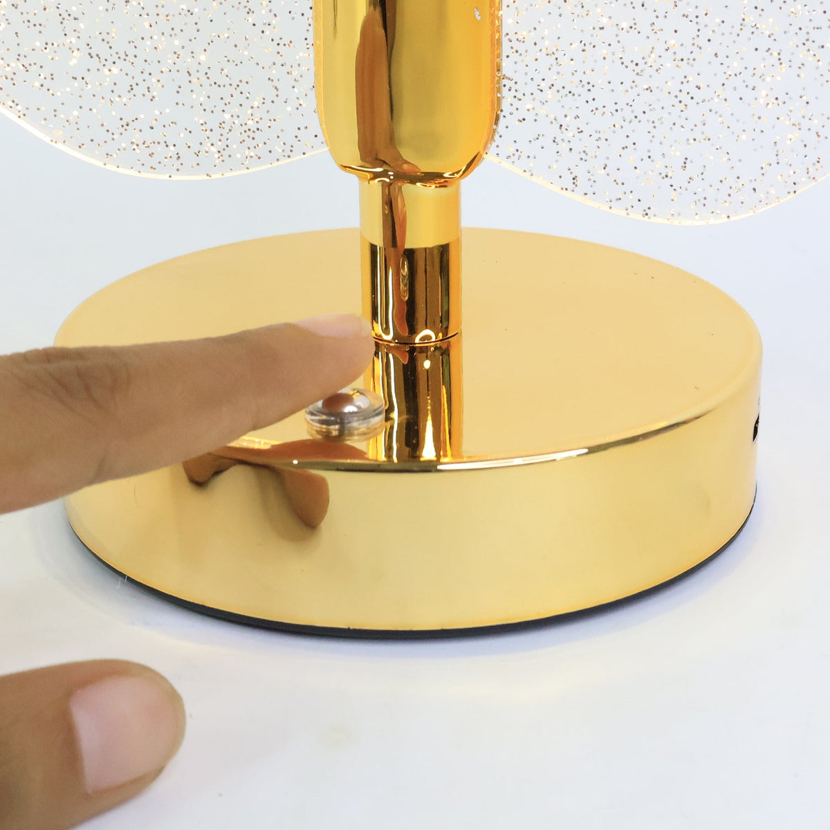 Close-up of a finger pressing the touch sensor on the gold, circular base of the lamp.