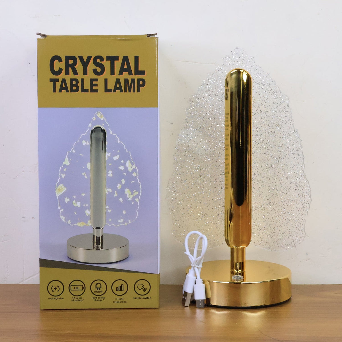 Crystal leaf lamp with a gold base and stem next to its product box on a light wooden surface.