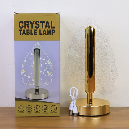 Crystal leaf lamp with a gold base and stem next to its product box on a light wooden surface.