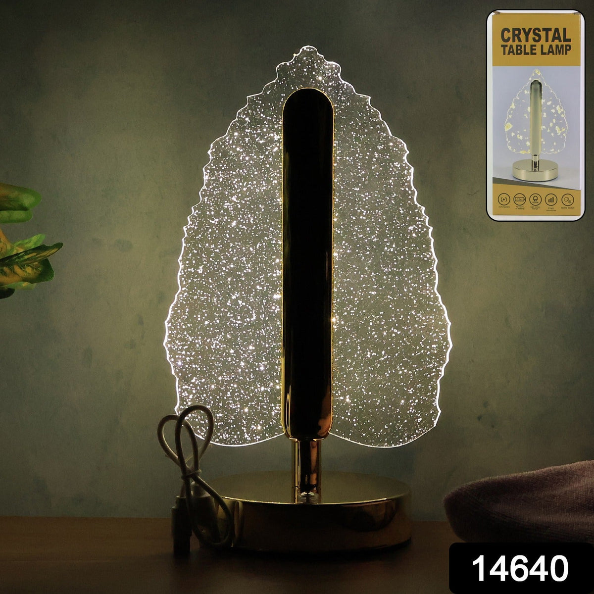 Crystal leaf lamp with gold base and stem, glowing on a dark surface, with product packaging in the corner.