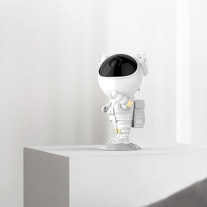 A white astronaut projector with a black visor stands on a white shelf against a plain white wall.