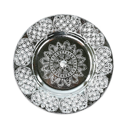 A top-down view of a round, silver-colored plastic pooja thali with intricate embossed patterns and a filigree edge.